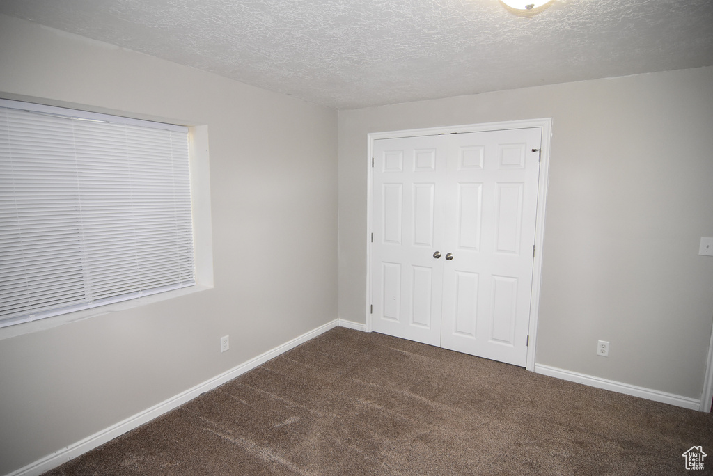 Unfurnished bedroom with carpet floors, a textured ceiling, a closet, and baseboards