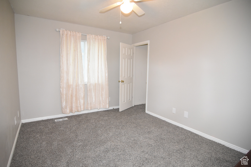 Carpeted empty room with a ceiling fan and baseboards