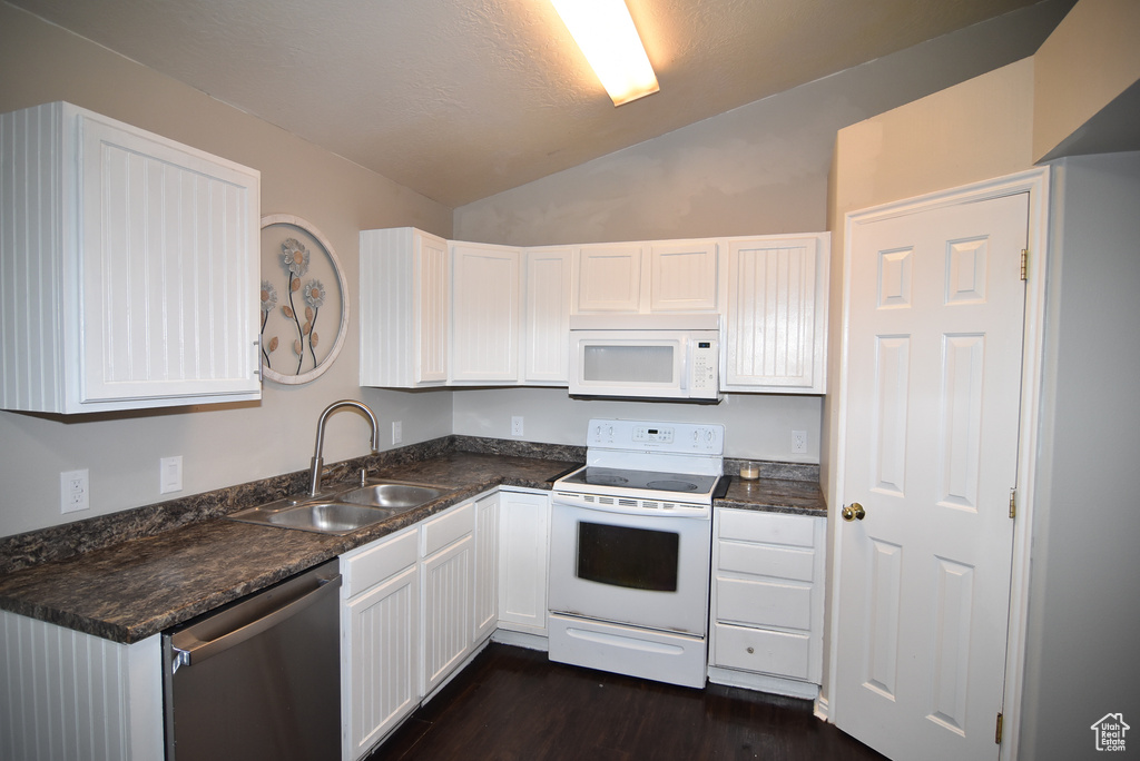 Kitchen with white appliances, a sink, lofted ceiling, white cabinets, and dark countertops