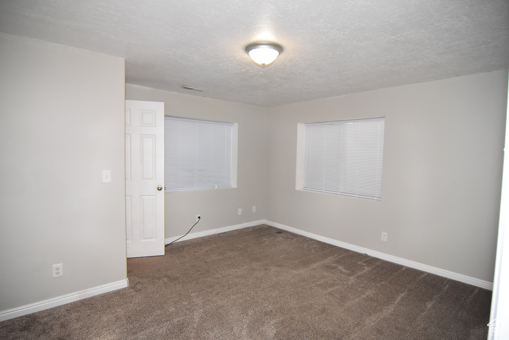 Unfurnished room featuring dark carpet, a textured ceiling, and baseboards