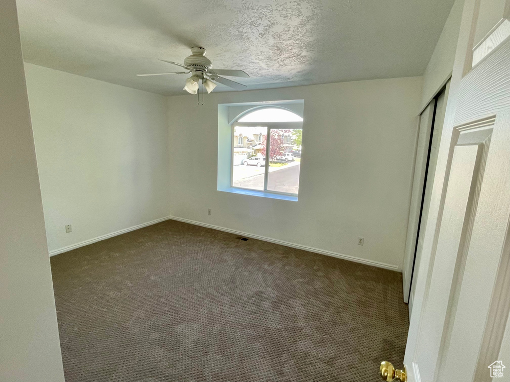 Unfurnished bedroom featuring dark colored carpet, a closet, and a ceiling fan