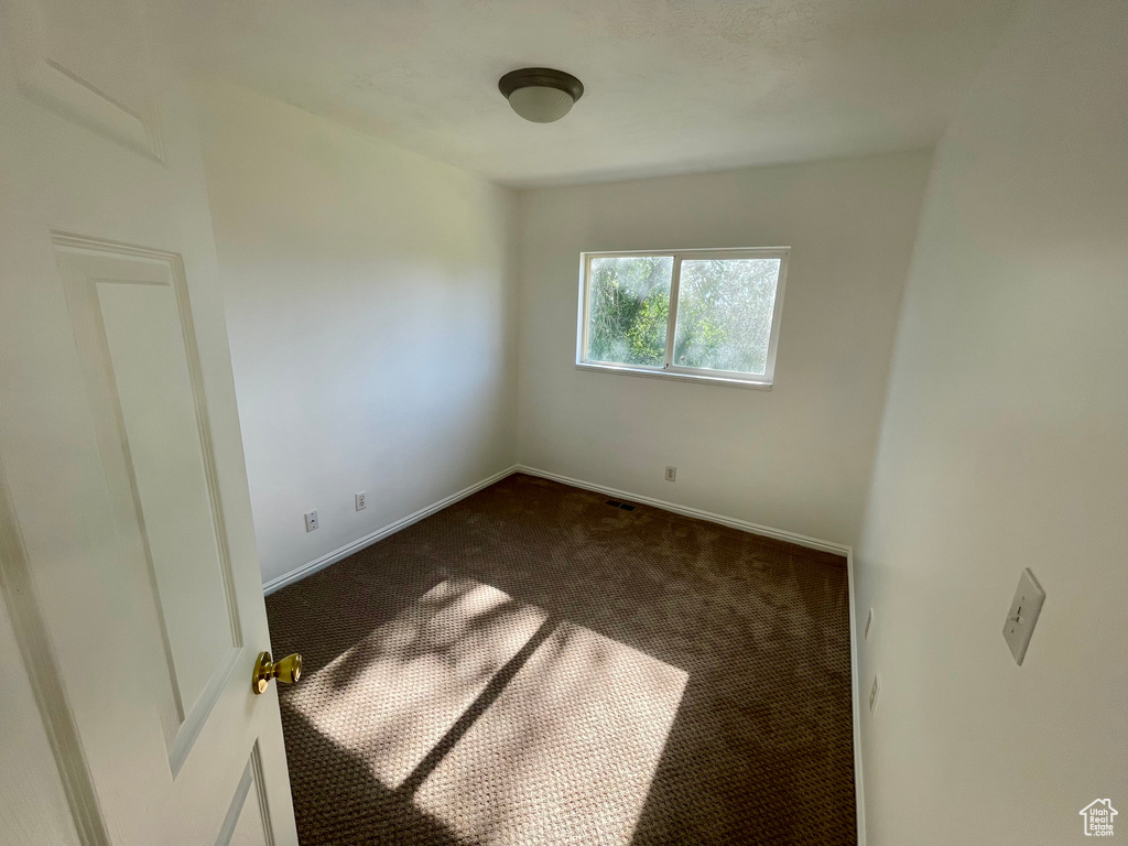 Spare room featuring dark carpet and baseboards