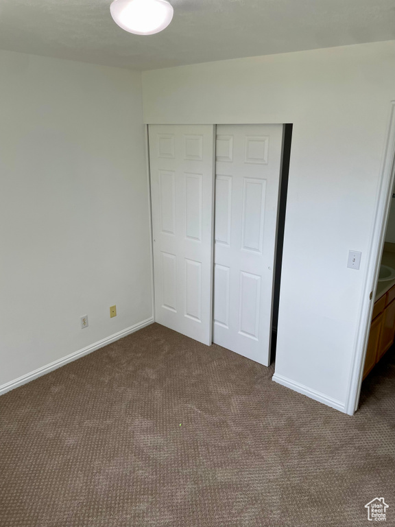 Unfurnished bedroom with dark colored carpet, a closet, and baseboards