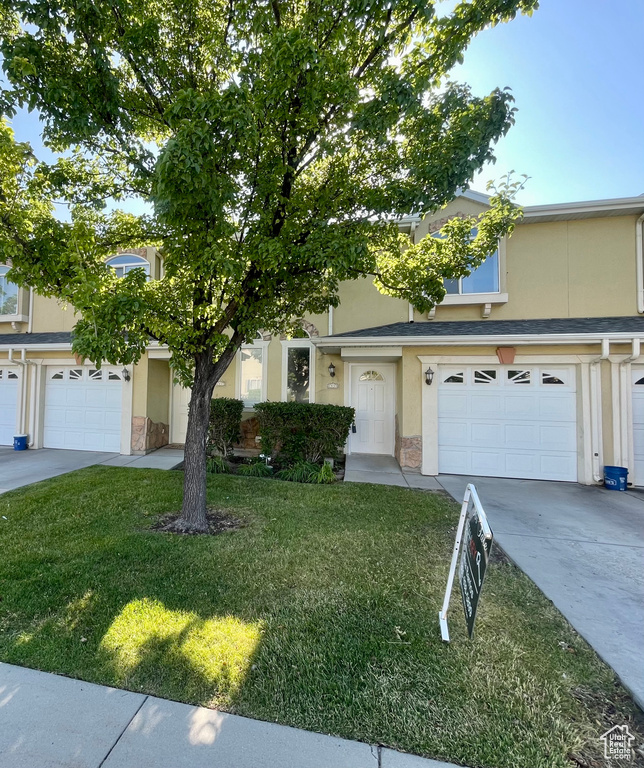 View of front of home with stucco siding, stone siding, a front lawn, and driveway