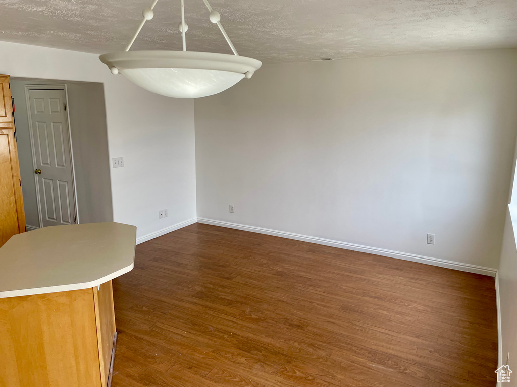 Unfurnished dining area with dark wood-type flooring, baseboards, and a textured ceiling