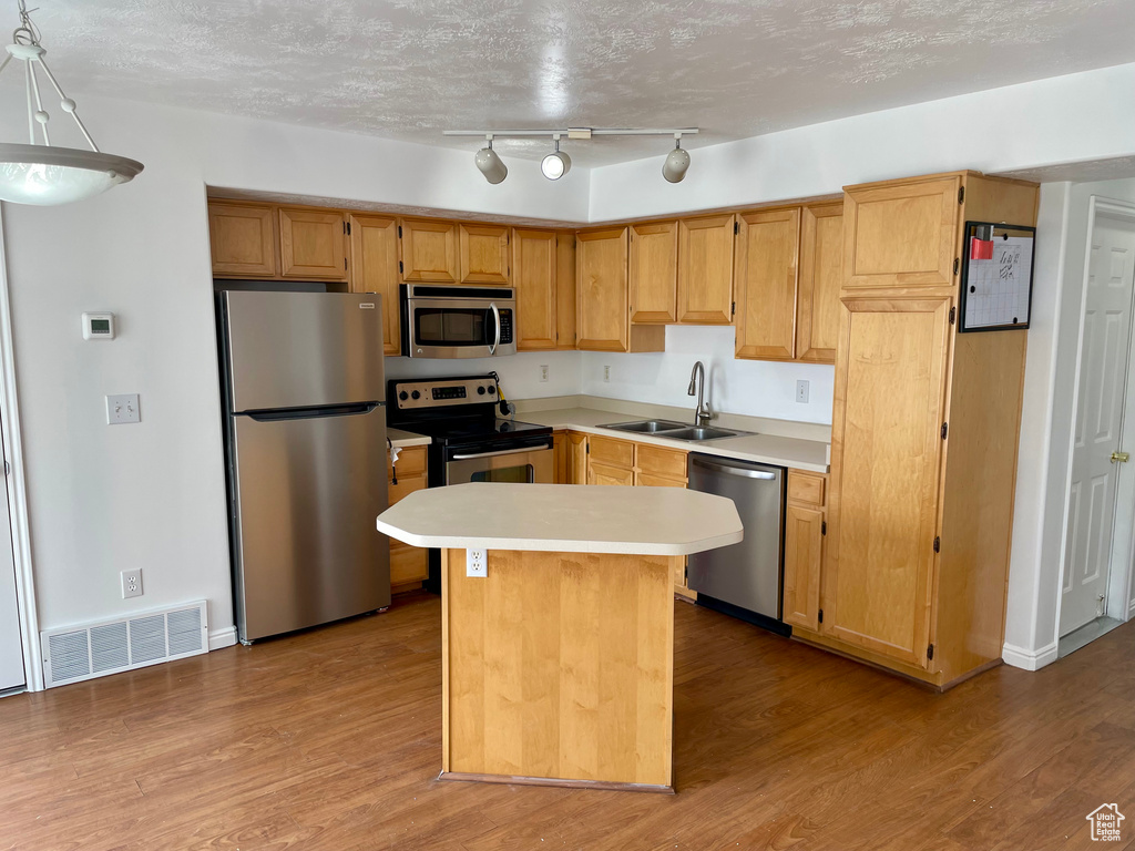 Kitchen with stainless steel appliances, a sink, light countertops, wood finished floors, and a center island