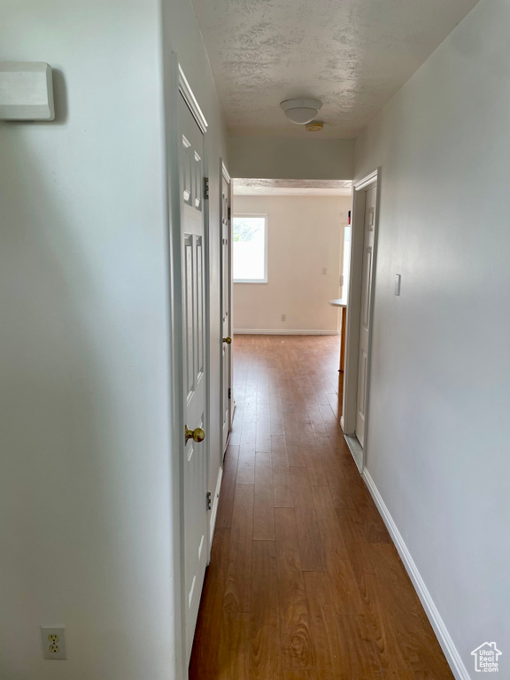 Hallway with dark wood finished floors, baseboards, and a textured ceiling