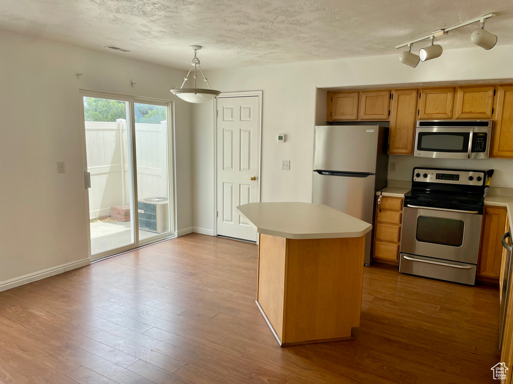 Kitchen featuring appliances with stainless steel finishes, light countertops, hardwood / wood-style floors, pendant lighting, and a textured ceiling