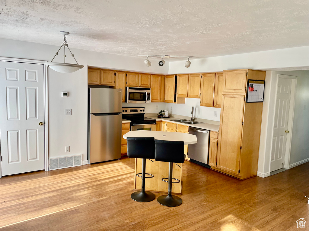Kitchen with stainless steel appliances, light countertops, light wood finished floors, a textured ceiling, and a kitchen breakfast bar