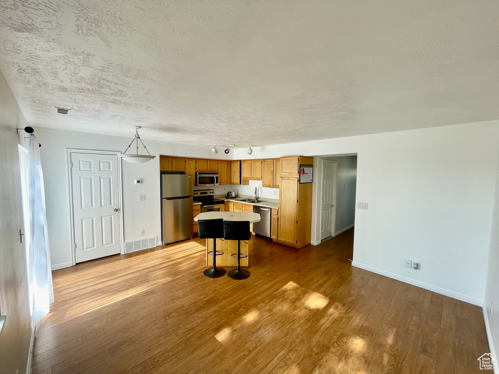 Kitchen featuring stainless steel appliances, light countertops, wood finished floors, a textured ceiling, and a center island