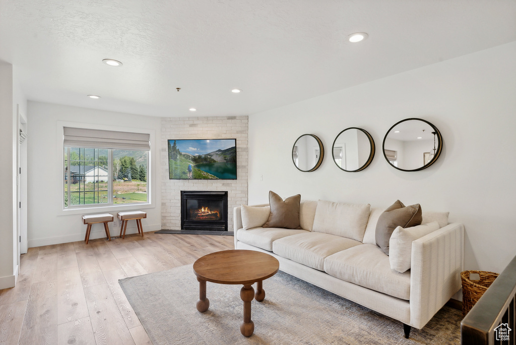 Living room featuring recessed lighting, baseboards, light wood-style flooring, and a brick fireplace