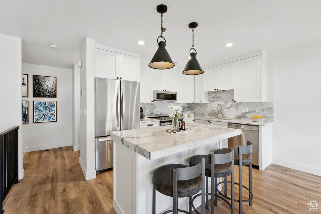 Kitchen with appliances with stainless steel finishes, baseboards, backsplash, a kitchen breakfast bar, and white cabinets