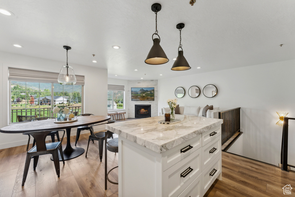 Kitchen featuring white cabinets, a kitchen island, a large fireplace, pendant lighting, and wood finished floors