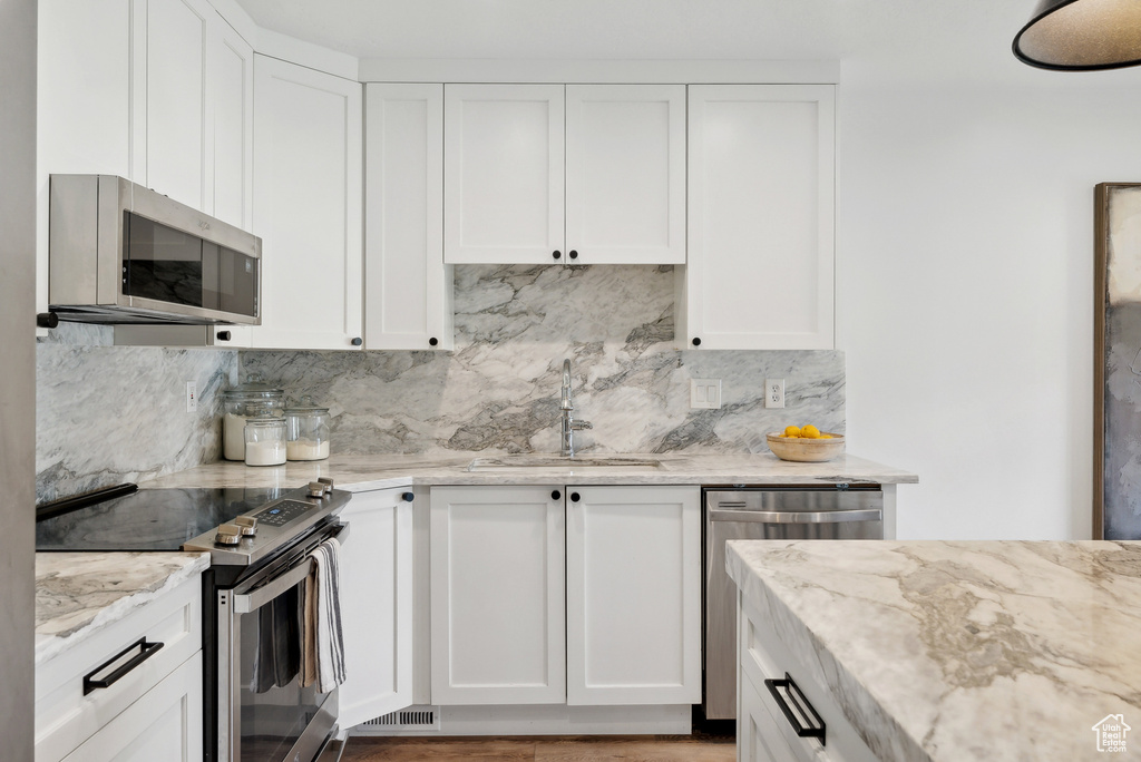 Kitchen with stainless steel appliances, a sink, backsplash, light stone counters, and white cabinets
