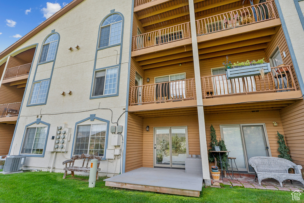 Back of property with a balcony, central air condition unit, and a lawn