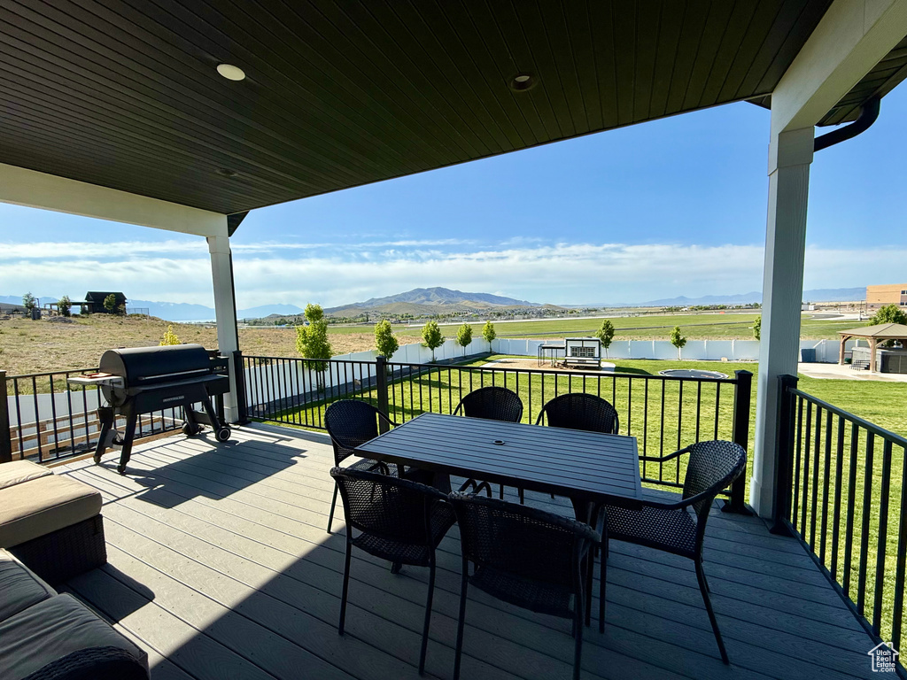 Wooden terrace featuring a water and mountain view, a grill, a yard, and outdoor dining space