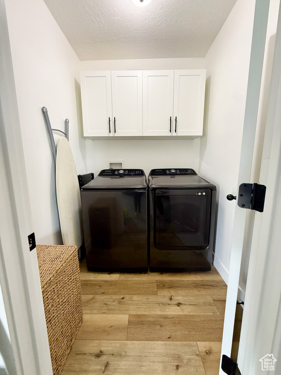 Laundry room with cabinet space, washing machine and clothes dryer, light wood-type flooring, and a textured ceiling
