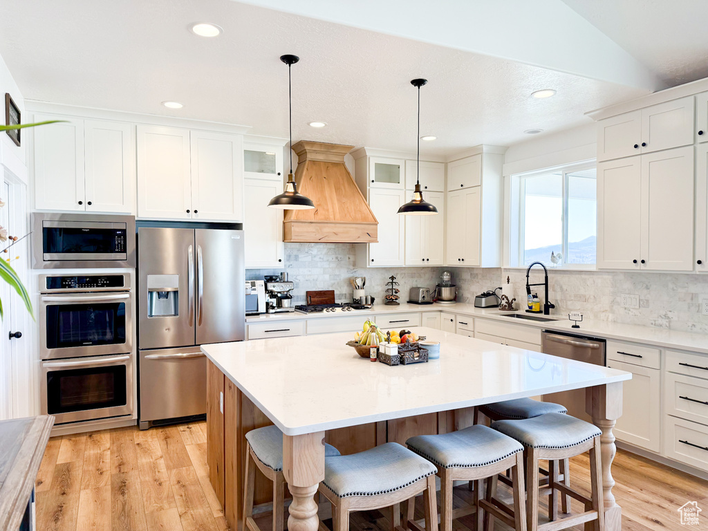 Kitchen featuring appliances with stainless steel finishes, a sink, custom exhaust hood, a breakfast bar, and light wood finished floors