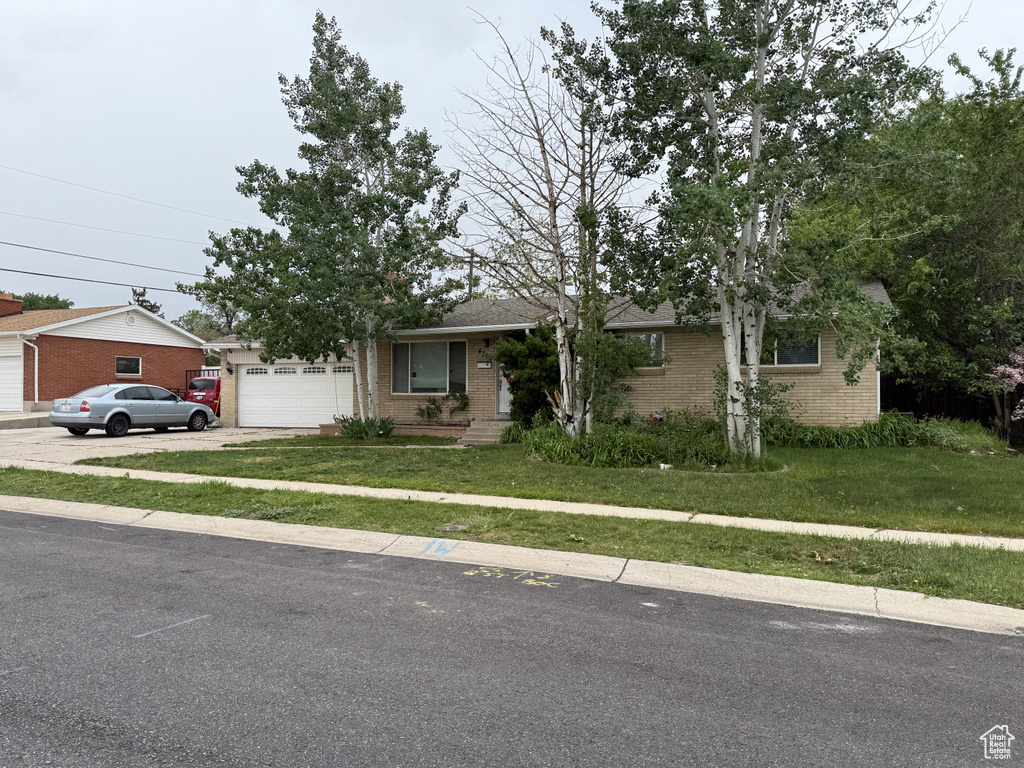View of front facade featuring brick siding, a front lawn, concrete driveway, and an attached garage