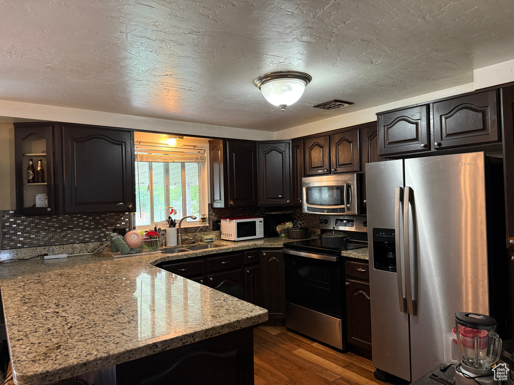 Kitchen featuring stainless steel appliances, a peninsula, a sink, light stone countertops, and backsplash