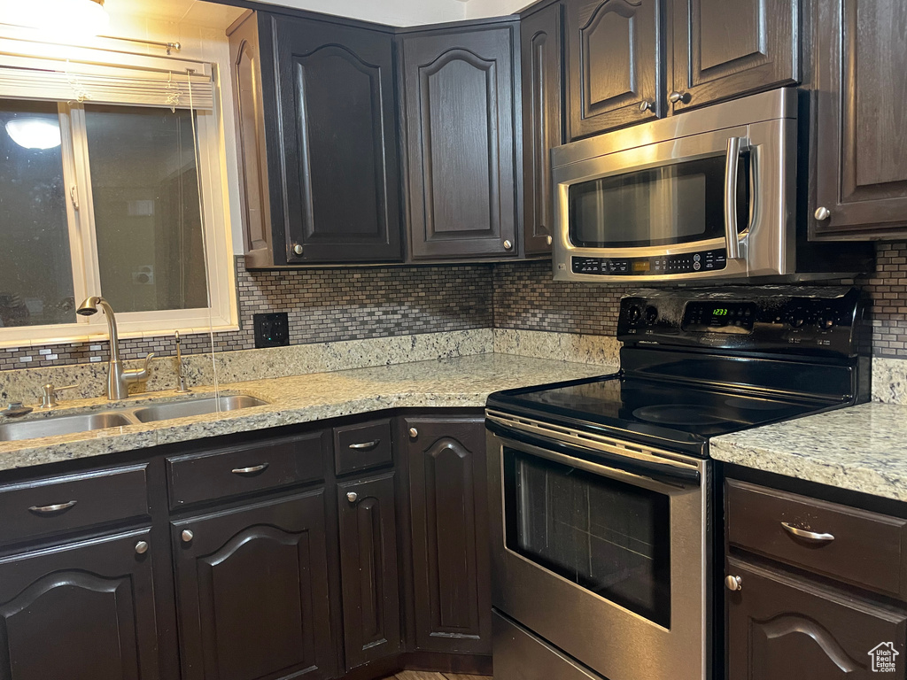 Kitchen featuring appliances with stainless steel finishes, a sink, tasteful backsplash, and light stone counters