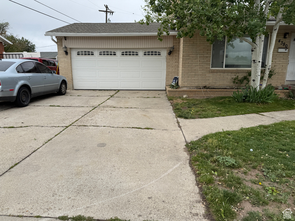 View of front of property featuring brick siding, an attached garage, driveway, and a shingled roof