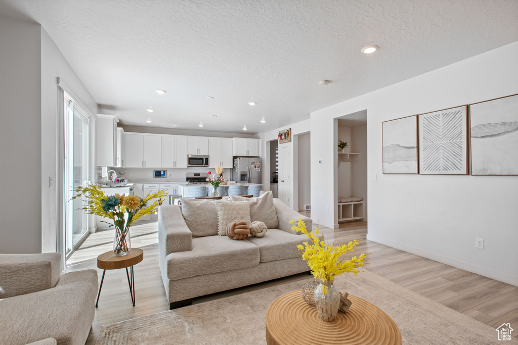 Living room featuring light wood-style flooring, a textured ceiling, recessed lighting, and baseboards