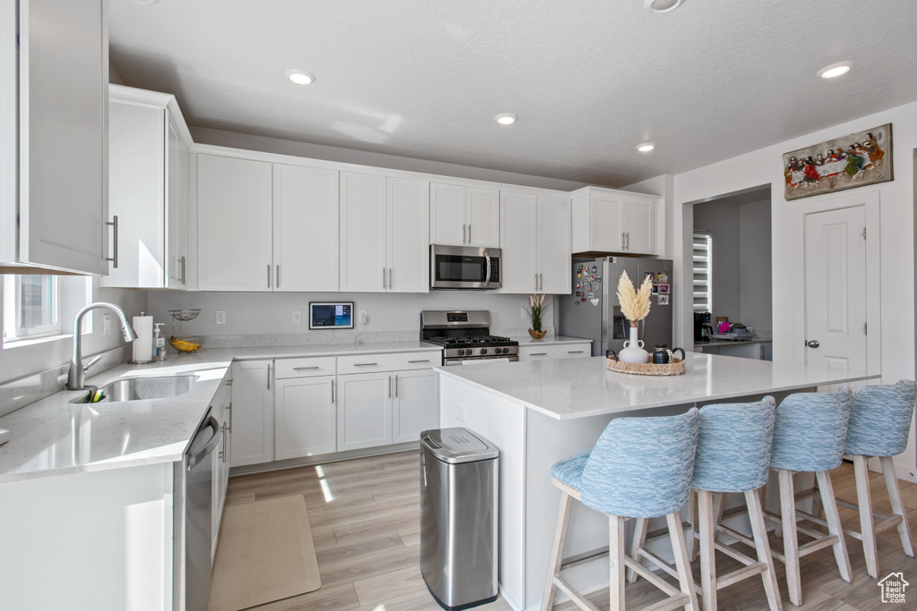 Kitchen with stainless steel appliances, a sink, light wood-style flooring, a kitchen bar, and a kitchen island