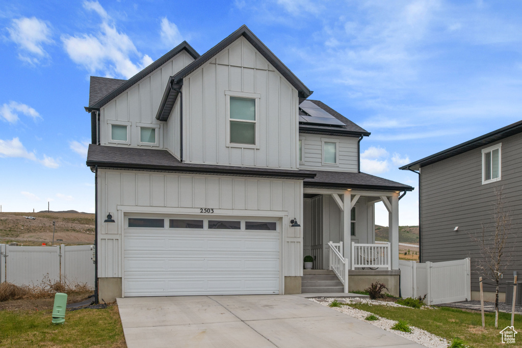 View of front of property with a porch, board and batten siding, an attached garage, driveway, and solar panels