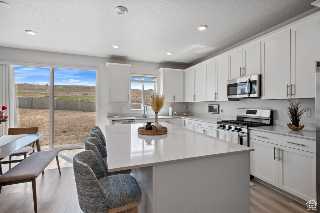 Kitchen featuring appliances with stainless steel finishes, a center island, a kitchen breakfast bar, a sink, and white cabinets