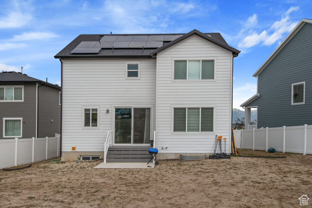 Rear view of house with entry steps, roof mounted solar panels, and a fenced backyard