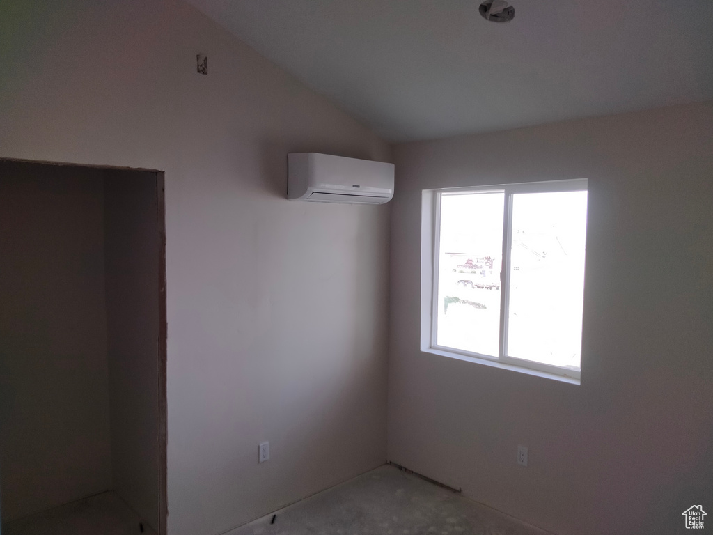 Empty room featuring an AC wall unit, plenty of natural light, and vaulted ceiling