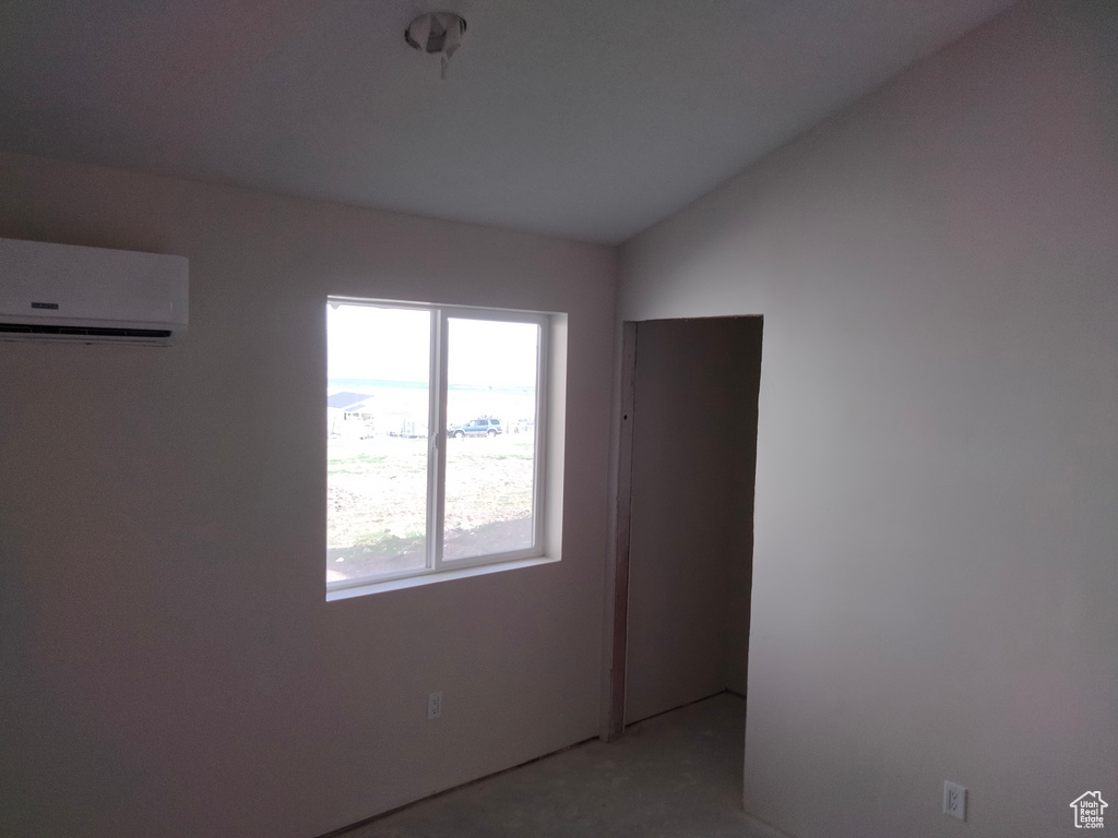 Unfurnished room featuring a wall mounted AC and vaulted ceiling