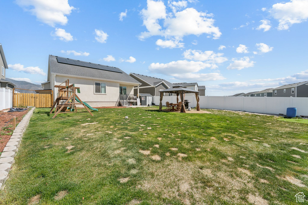 Back of house with a playground, a gazebo, a patio, stucco siding, and roof mounted solar panels