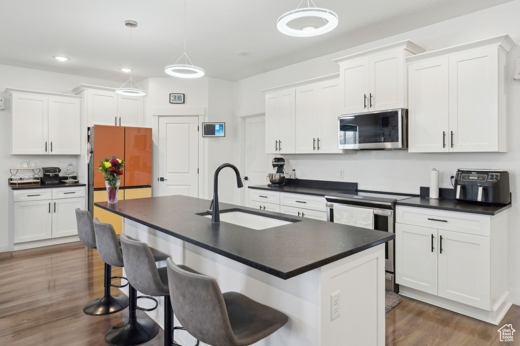 Kitchen with appliances with stainless steel finishes, a sink, dark countertops, dark wood-style floors, and white cabinetry
