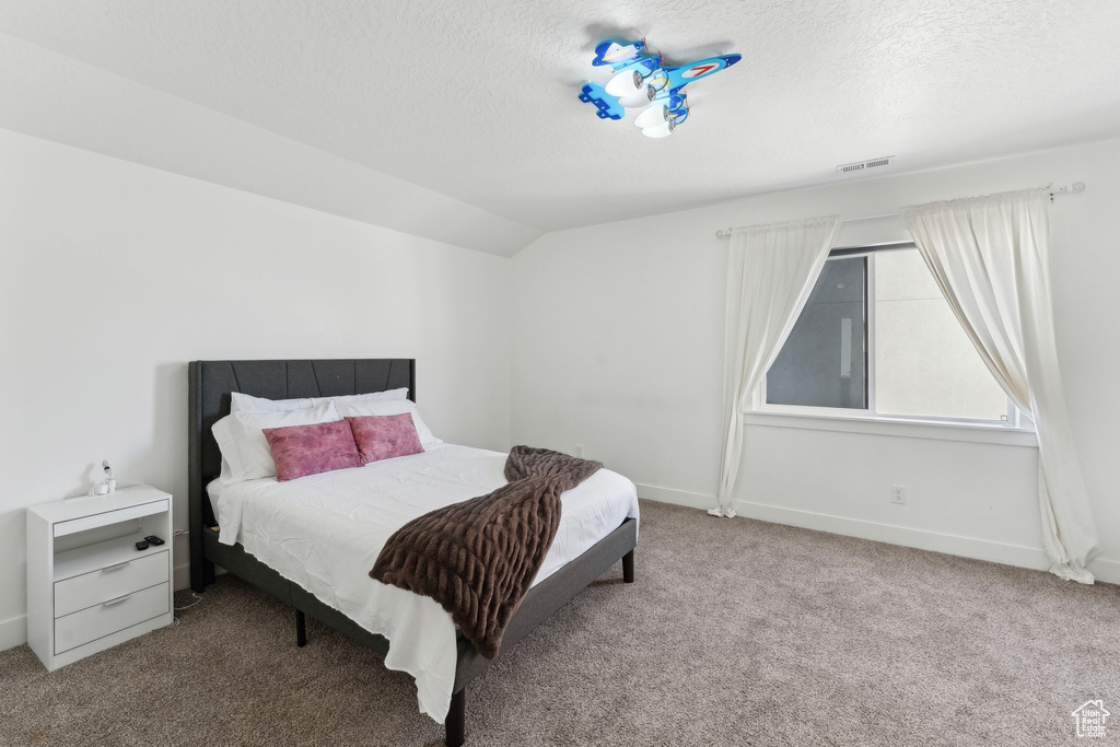 Bedroom with carpet, a textured ceiling, vaulted ceiling, and baseboards