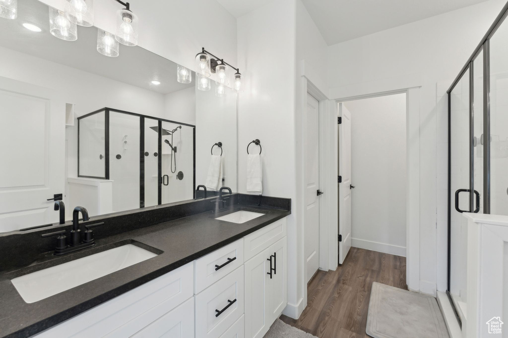 Full bath featuring a shower stall, double vanity, wood finished floors, and baseboards