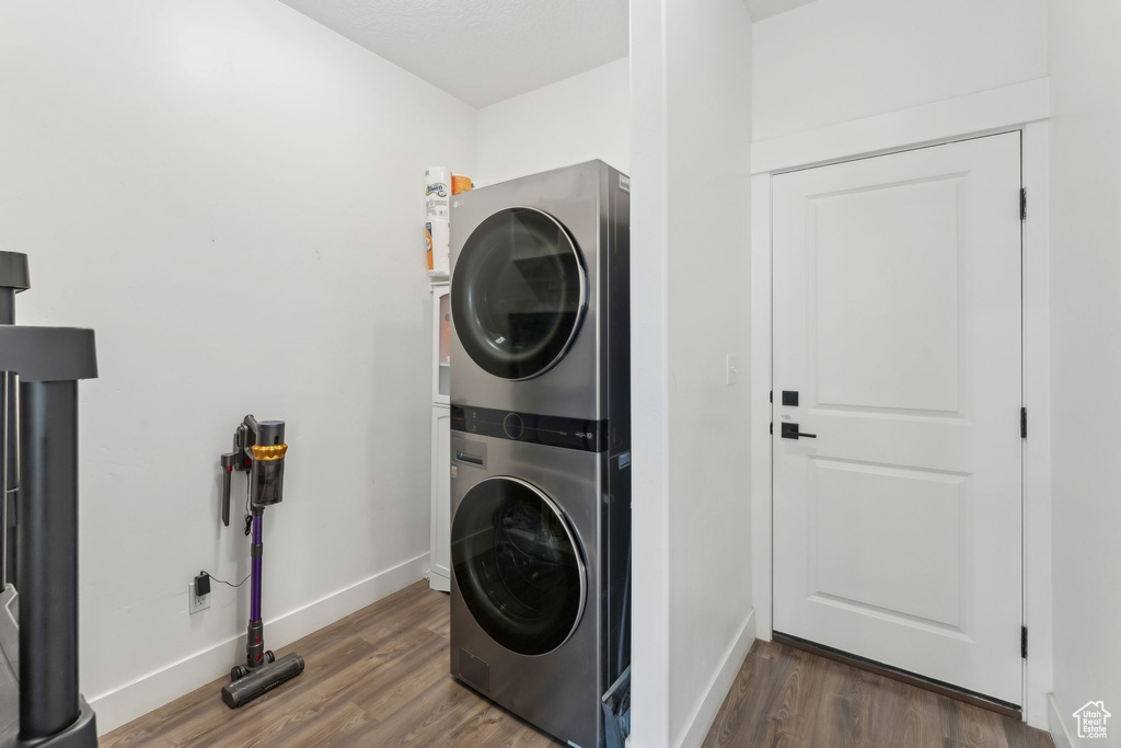 Laundry room with stacked washing machine and dryer, wood finished floors, and baseboards