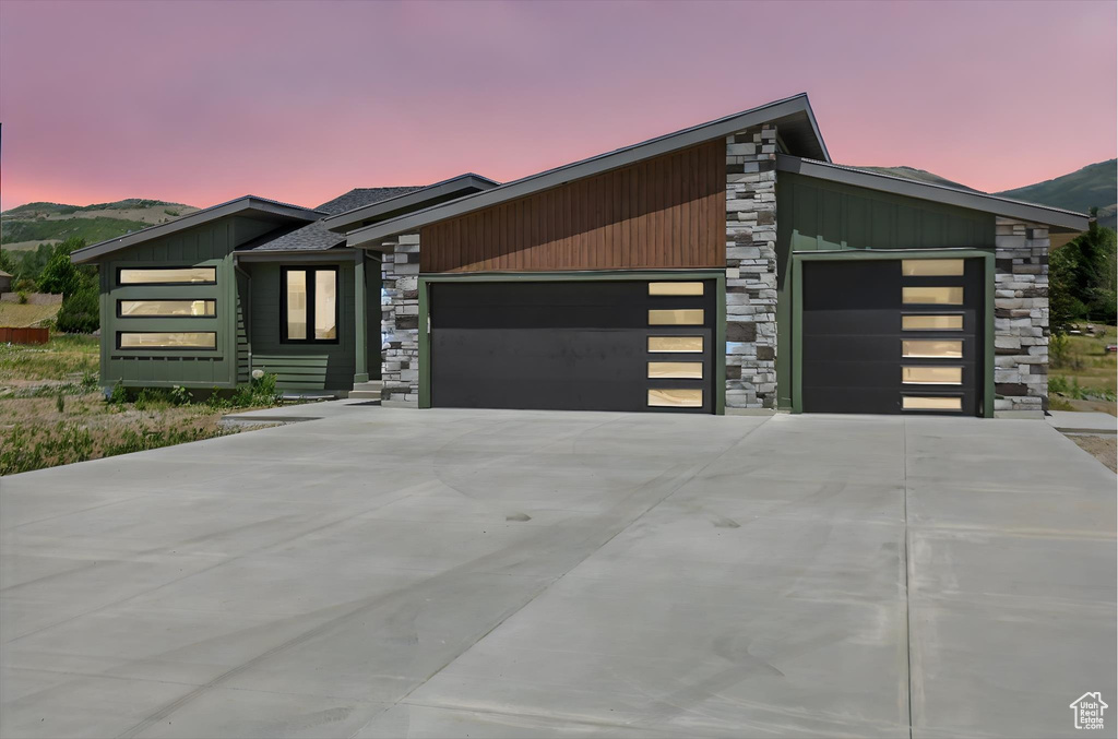 Contemporary home featuring stone siding, a garage, driveway, and a mountain view
