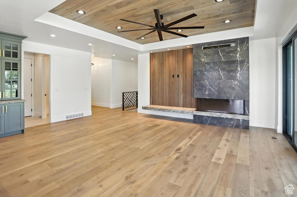 Unfurnished living room with a raised ceiling, wood ceiling, recessed lighting, light wood-style flooring, and a high end fireplace