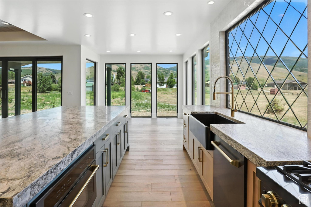 Kitchen with dishwasher, recessed lighting, light wood-style floors, light stone counters, and range