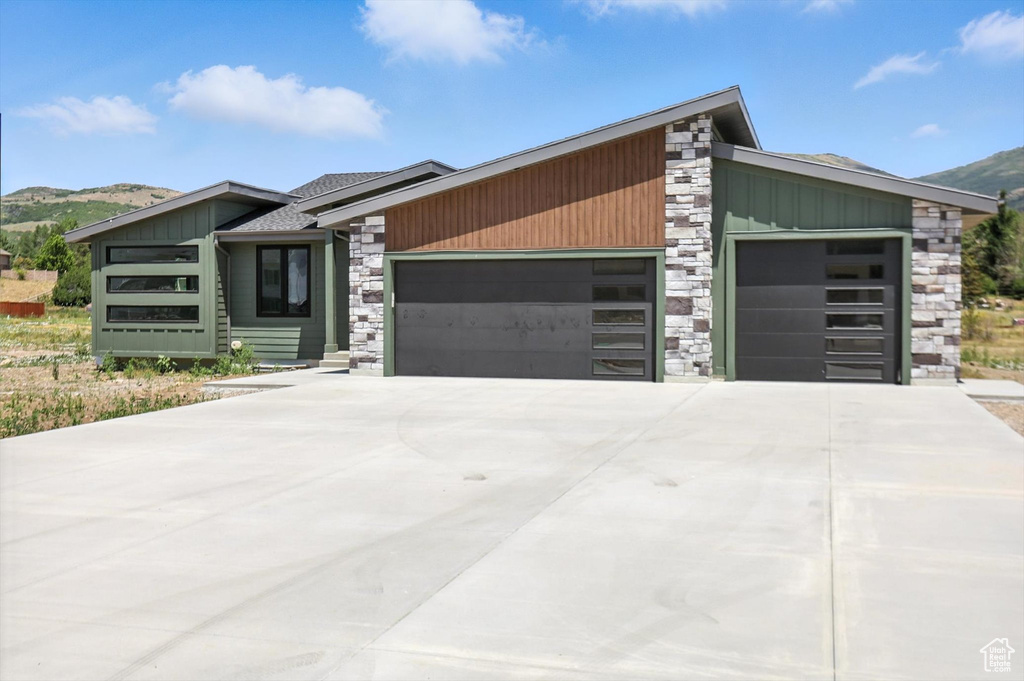 View of front facade featuring stone siding, a garage, board and batten siding, a mountain view, and concrete driveway