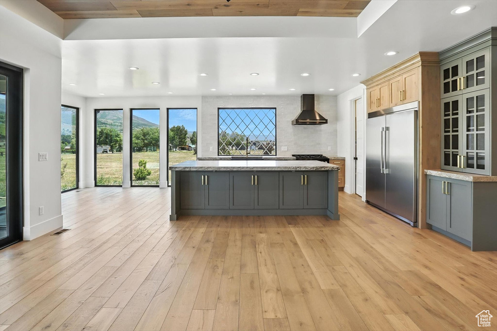 Kitchen with stainless steel built in refrigerator, wall chimney range hood, gray cabinets, light wood-style flooring, and recessed lighting