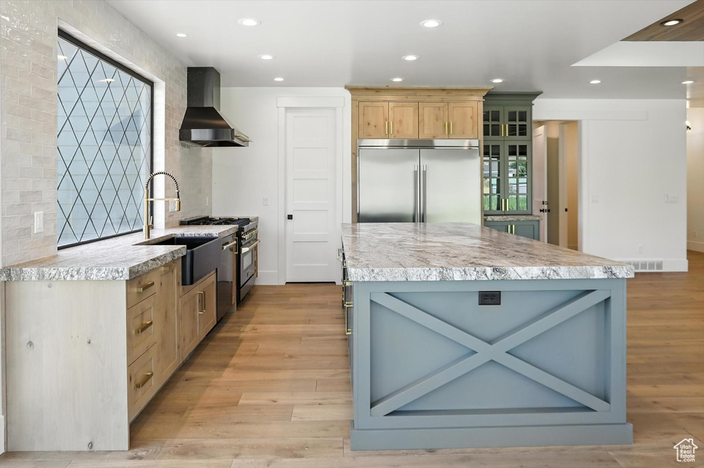 Kitchen with wall chimney range hood, premium appliances, light countertops, light wood-style flooring, and recessed lighting