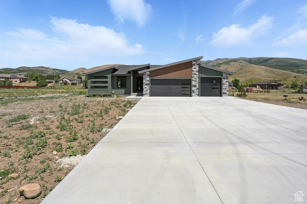 Modern home featuring a mountain view, a garage, stone siding, and driveway