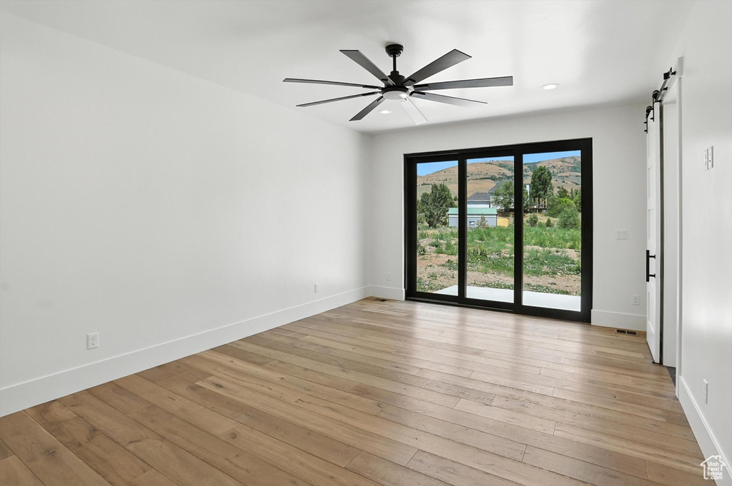 Spare room featuring a barn door, ceiling fan, light wood-style flooring, and recessed lighting