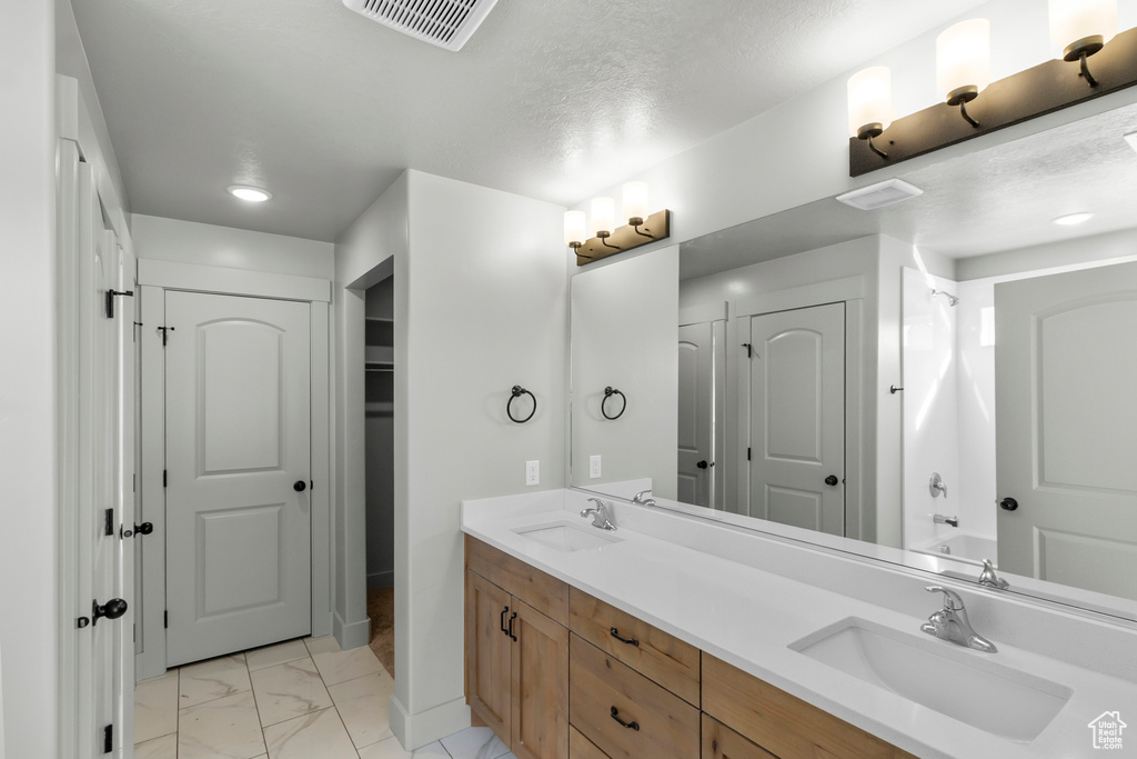 Bathroom featuring a closet, marble look tile flooring, double vanity, and bathtub / shower combination
