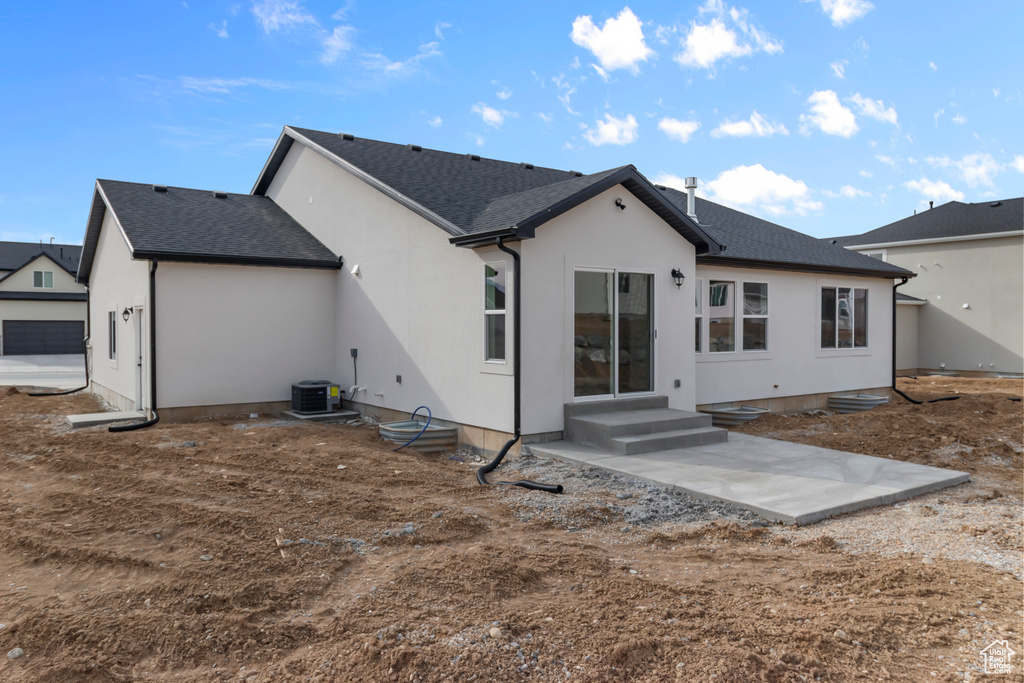 Back of house featuring roof with shingles, stucco siding, central air condition unit, and a patio area