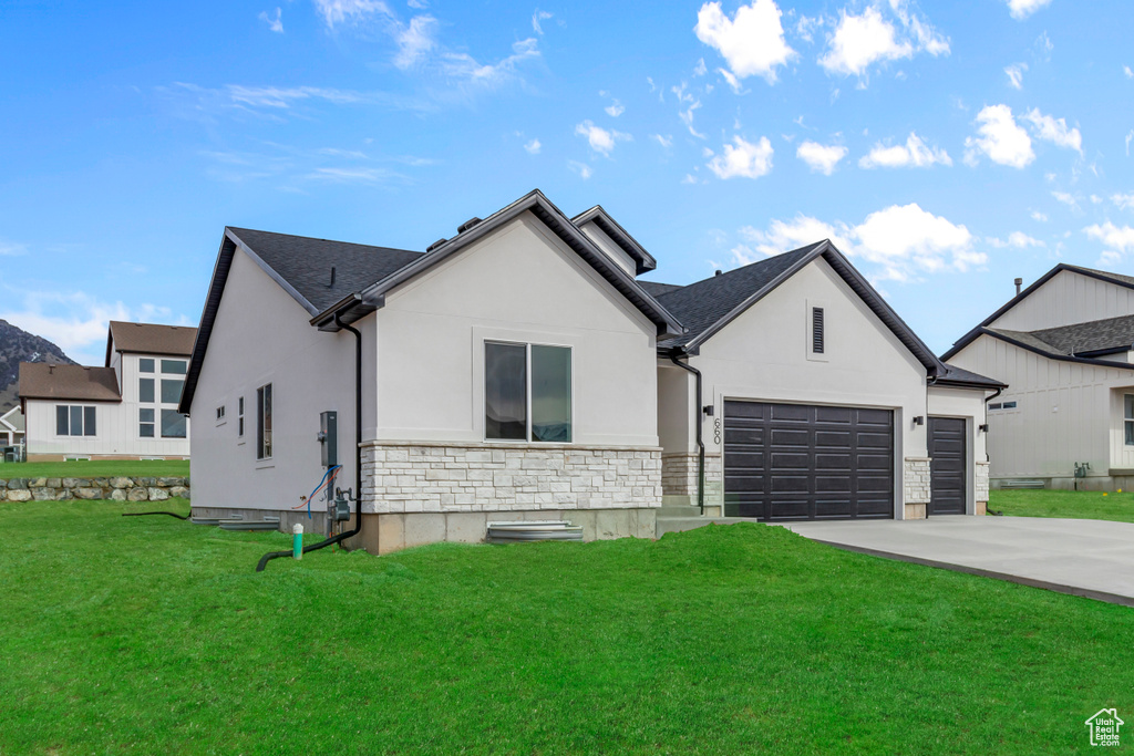 View of front of property with stucco siding, concrete driveway, a front lawn, an attached garage, and stone siding