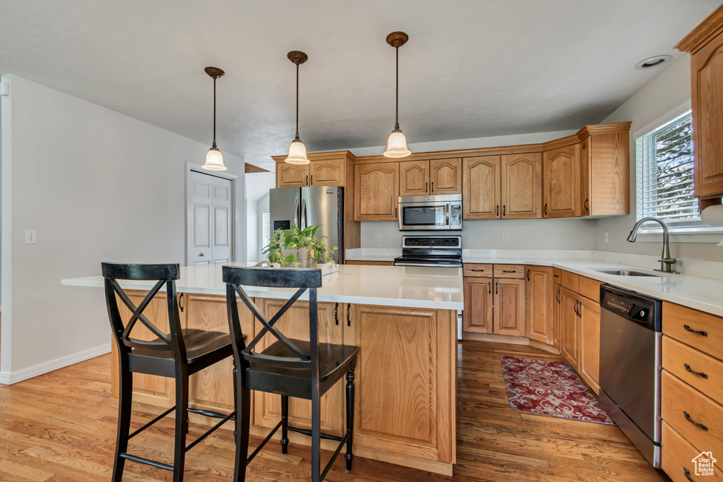 Kitchen with stainless steel appliances, a sink, light wood-style flooring, a center island, and a kitchen bar